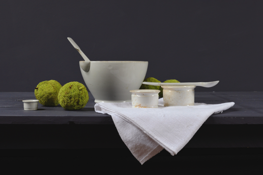 Realistisch stilleven met wit servies, linnen doek en groene Osagedoorn-vruchten – fine art print van Dirk Bal.
