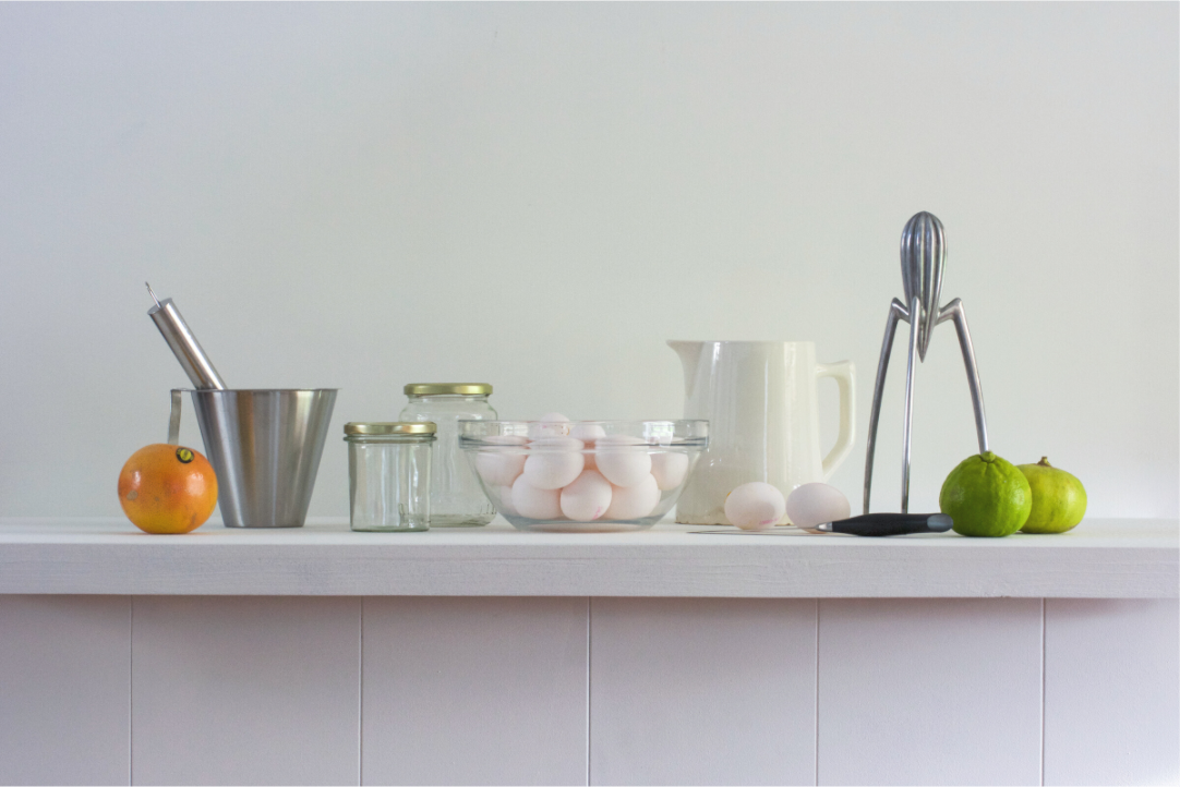 Realistisch stilleven van keukengerei en ingrediënten, inclusief eieren, glazen potten, een citruspers, een sinaasappel en limoenachtige vruchten. Kunstwerk van Dirk Bal