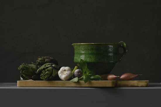 Realistisch stilleven van artisjokken, knoflook, basilicum en sjalotten met groene kom – fine art print van Dirk Bal.