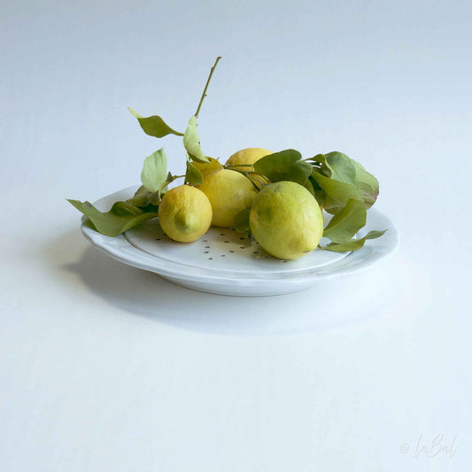 Realistisch stilleven van biologische citroenen met blad op wit bord – fine art print van Dirk Bal.