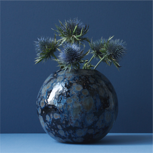 Realistisch stilleven van blauwe distels in een ronde keramieken vaas met blauw-zwarte glazuur, gefotografeerd door Dirk Bal.
