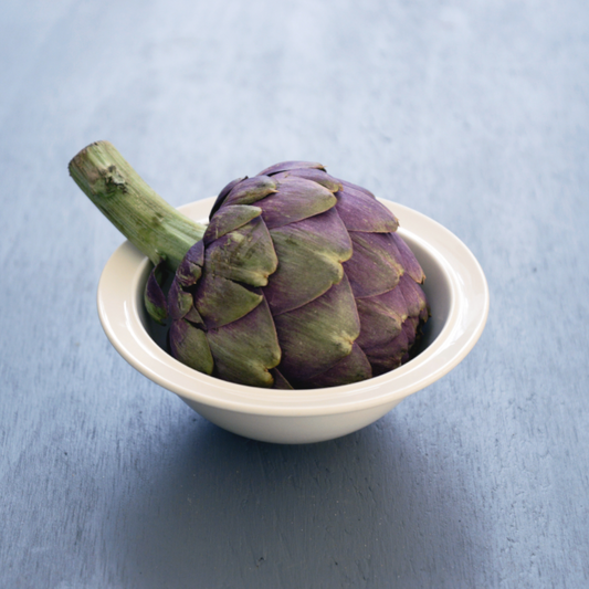 Realistisch stilleven van paarse artisjok in witte schaal op blauwe achtergrond – fine art print van Dirk Bal.