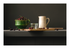 Stilleven met groene kom vol kersen, roomkleurige kan, glazen pot en houten lepel op donkere achtergrond.